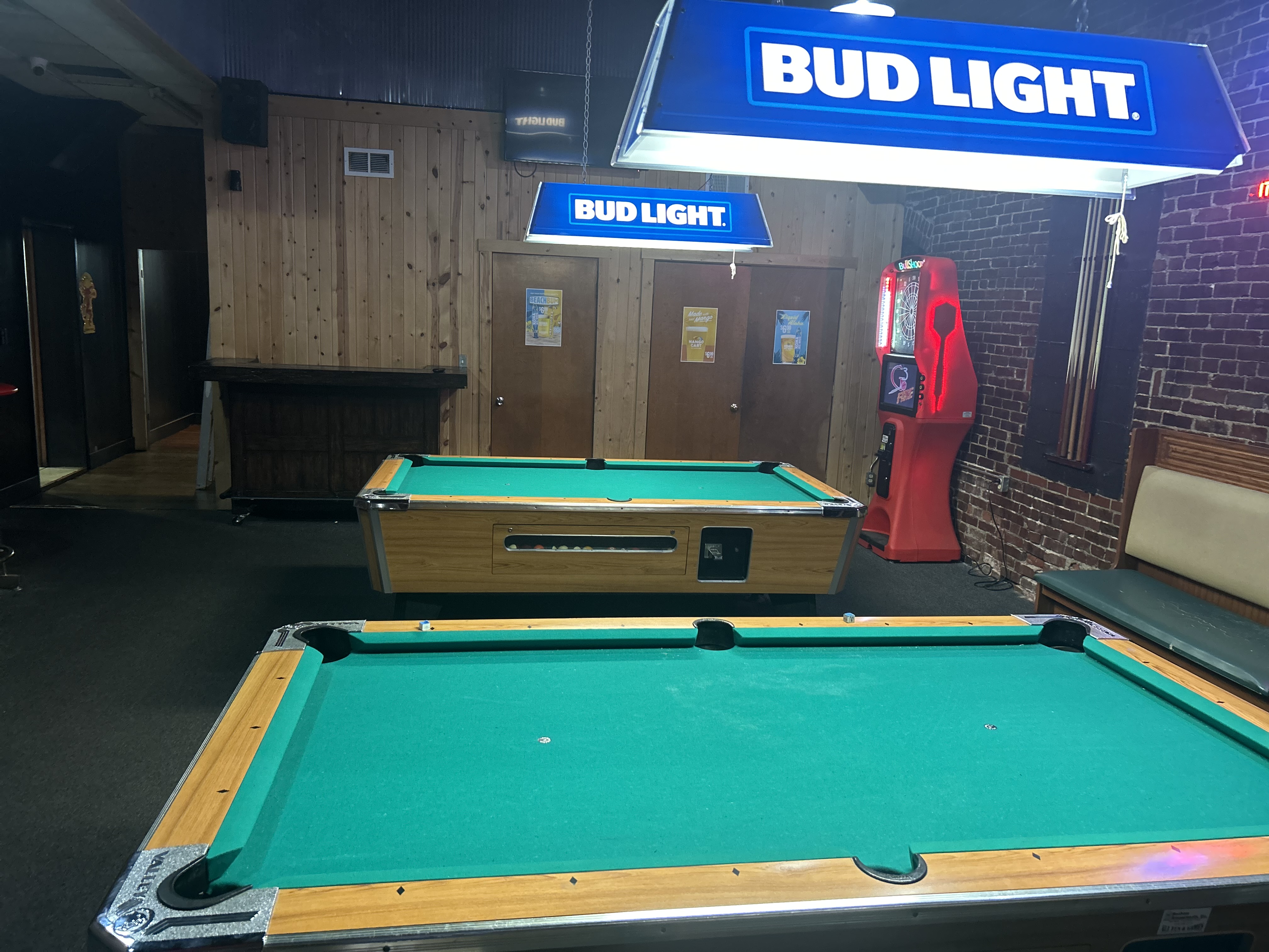 Pool room at The Vault — Bud Light signs overhead, dart machine, brick and wood paneling